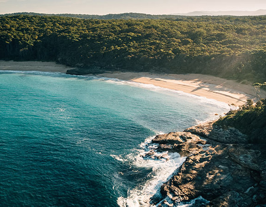 Aerial view of turquoise water, beach and forest near South Durras